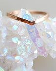 A rose gold chevron ring on a bed of iridescent white crystals.