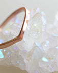 A rose gold curved band ring. The ring is sitting on a cluster of white quartz crystals.