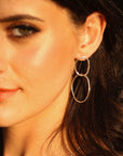 A woman wearing a pair of silver double hoop earrings. The earrings are made of two connected oval shapes.