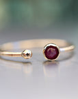 A gold ring with a single red garnet gemstone. The ring is open on one side and has a small ball on the other side.