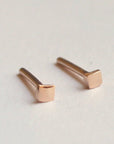 Two small, square-shaped earrings made of rose gold. The earrings are simple and minimalist in design.