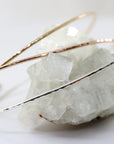 Three delicate hammered gold bangles, one silver, one gold, and one rose gold, are stacked on a white crystal rock.