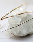 Three delicate hammered gold bangles, one silver, one gold, and one rose gold, are stacked on a white crystal rock.