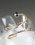 A gold spiral ring with a blue gemstone. The ring is textured and has a hammered finish.
