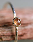 A delicate gold ring with a hammered band and a small, round, orange gemstone.
