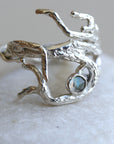 A silver ring with a textured, branch-like design and a blue-green gemstone in the center.