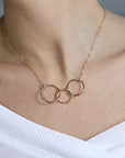 A gold necklace with three interlocking circles. The circles are slightly textured and have a hammered finish.