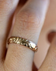 A gold band ring with a floral design. The ring is worn on a person&