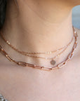 A layered rose gold necklace with a delicate chain and a larger, chunky chain with a small circular pendant.