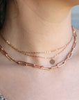 A layered rose gold necklace with a delicate chain and a larger, chunky chain with a small circular pendant.