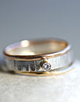 Set of three rings. A silver and rose gold band ring with a single diamond set in the center. The ring has a textured finish.