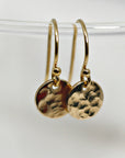 A pair of gold hammered disc earrings with a simple hook closure.