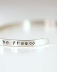 Silver bangle bracelet with the words "things be free" and a heart symbol engraved on it.
