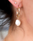 Gold hoop earrings with a large white pearl dangling from one earring.