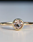 A delicate gold ring with a round, bezel-set, pale pink morganite gemstone.