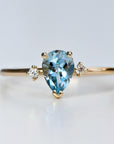 A gold ring with a pear-shaped aquamarine gemstone and two smaller round diamonds on the band.