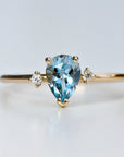 A gold ring with a pear-shaped aquamarine gemstone and two smaller round diamonds on the band.
