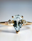 A pear-shaped aquamarine gemstone ring set in gold with two smaller diamond accents.