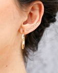 pair of gold hoop earrings and a gold bar earring. The hoop earrings are hammered and have a slightly irregular shape. The bar earring is straight and has a hammered texture.