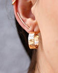 Gold hammered hoop earrings. The earrings are thick and have a hammered texture. The earrings are shown on a model&