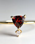 A gold ring with a triangular red garnet gemstone and a smaller round clear gemstone hanging below.