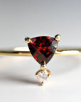 A gold ring with a triangular red garnet gemstone and a smaller round clear gemstone hanging below.