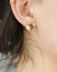 A pair of gold hammered disc earrings. The earrings are small and round, with a textured surface.