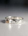 A silver ring with a hammered texture and a small gold bead accent.