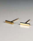 A pair of gold bar stud earrings. The earrings are simple and minimalist, with a straight bar design.