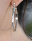 Silver hoop earrings with a floral design. The earrings are large and have a polished finish.