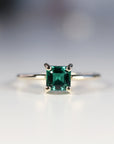 A gold ring with a square emerald green emerald gemstone set in a four-prong setting.