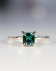 A gold ring with a square emerald green emerald gemstone set in a four-prong setting.