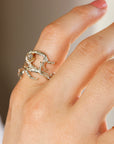 A gold ring with a textured, branch-like design and a clear gemstone in the center.