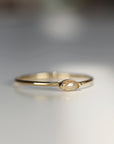 A gold band ring with a small, light brown, marquise-shaped diamond