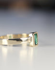 A gold ring with a green emerald gemstone set in a square bezel setting.