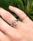 Teardrop aquamarine gold ring with tiny diamond accent paired with thin gold stacking band, minimalist gemstone ring set on hand with natural green background