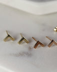 Four gold and rose gold chevron shaped earrings on a white marble surface.