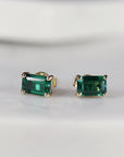 A pair of gold earrings with emerald green rectangular emerald gemstones.