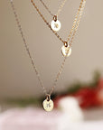 A gold necklace with three small, round pendants. The pendants are engraved with the letters "M", "R", and "B".
