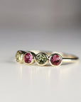 A gold band ring with four round gemstones. The gemstones are alternating colors of pink and green.