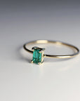 A delicate gold ring with a single emerald green gemstone set in a rectangular shape.