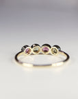May include: A gold band ring with four round gemstones. The gemstones are pink, green, pink, green, and green.