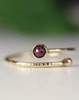 A delicate gold ring with a textured band and a single, deep red gemstone set in the center.