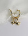 Two gold hoop earrings with a dangling star charm. The hoops are lined with small clear diamond stones and the stars have a single clear diamond stone in the center.
