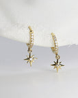 A pair of gold hoop earrings with a dangling star charm. Each hoop is lined with small clear stones and the star charm has a single clear stone in the center.