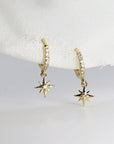 A pair of gold hoop earrings with a dangling star charm. Each hoop is lined with small clear stones and the star charm has a single clear stone in the center.