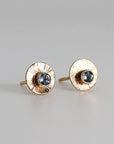 A pair of gold earrings with a textured circular design and a small blue aquamarine gemstone in the center of each earring.