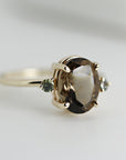 A gold ring with a large oval-shaped brown gemstone and two smaller round green gemstones on either side.