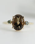 An 14K gold ring with a large oval brown Quartz gemstone and two smaller round green sapphire gemstones on either side.