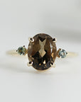 An 14K gold ring with a large oval brown Quartz gemstone and two smaller round green sapphire gemstones on either side.